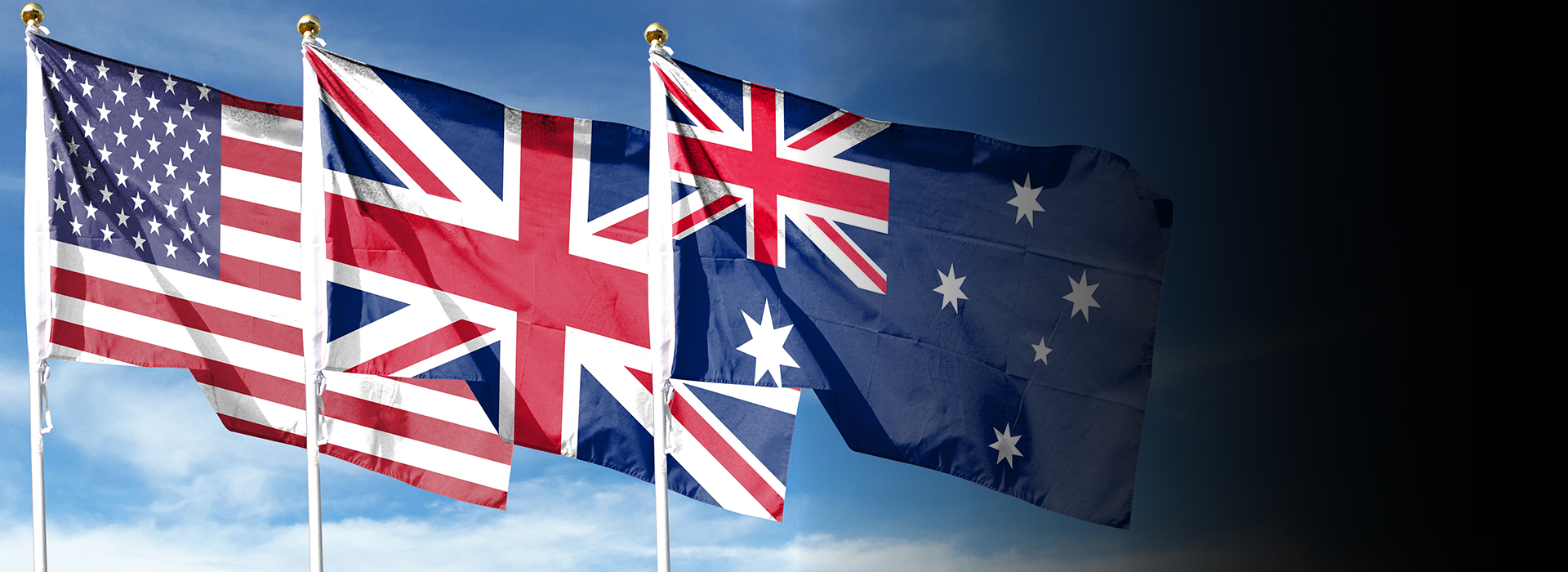US, UK and Australian flags flying against blue sky