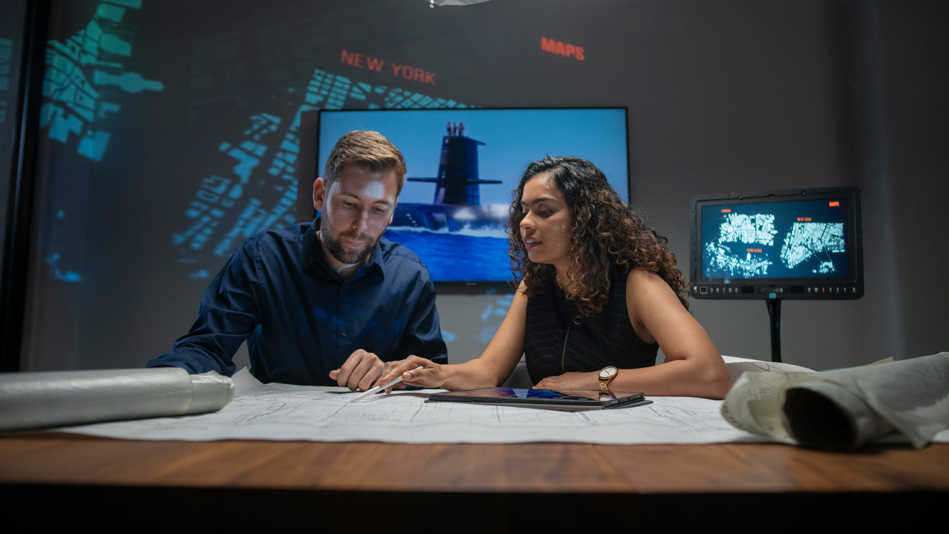 Young man and woman working in the defence industry talking over blueprints