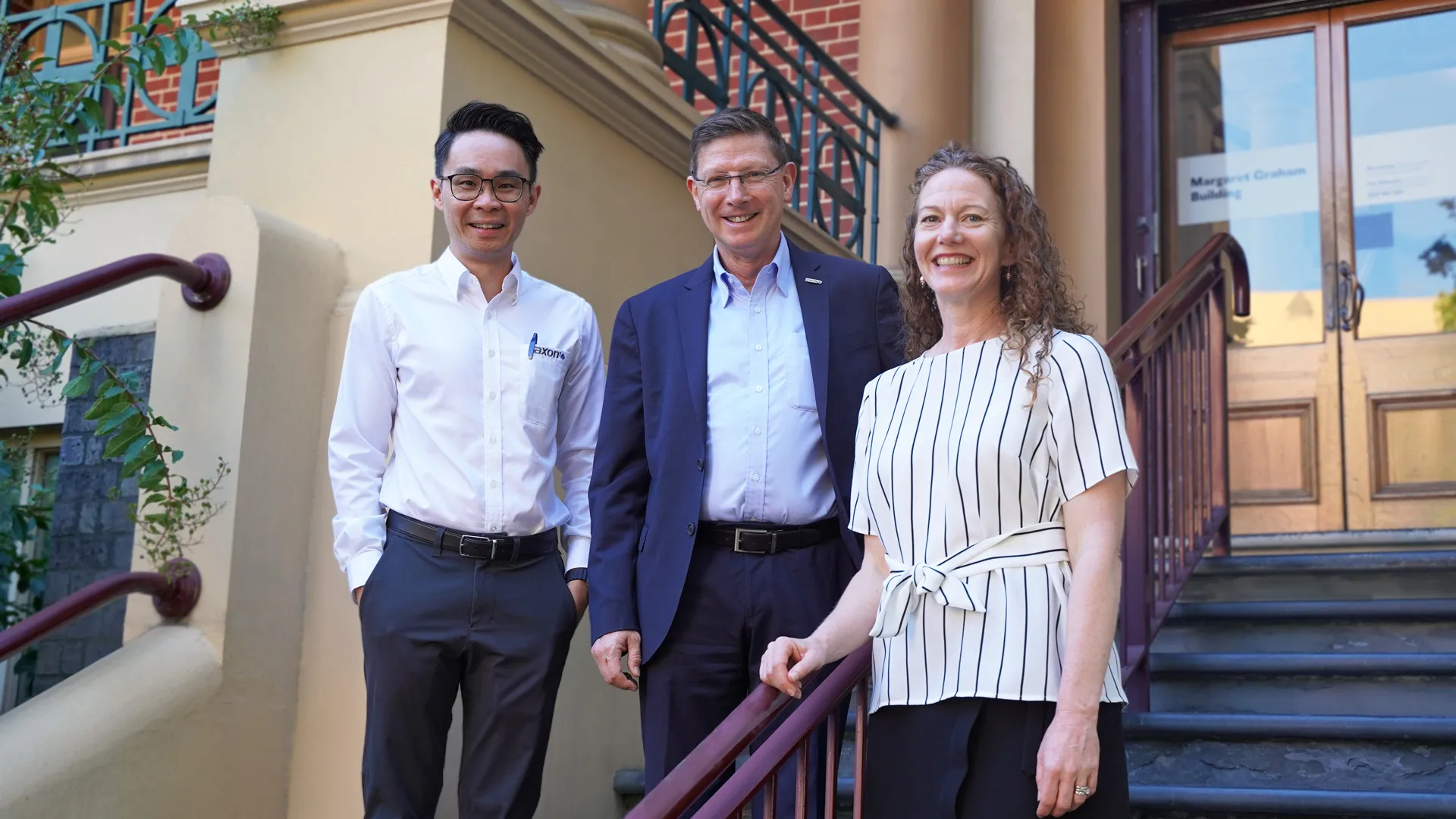 Axon Global Business Development Manager Hung‑Peng Koay with Global Manager Stéphane Watier and Defence SA Director Corporate Services Ilona Horan — Photo 1 copy Two men and a woman stand on the steps of a building smiling at the camera