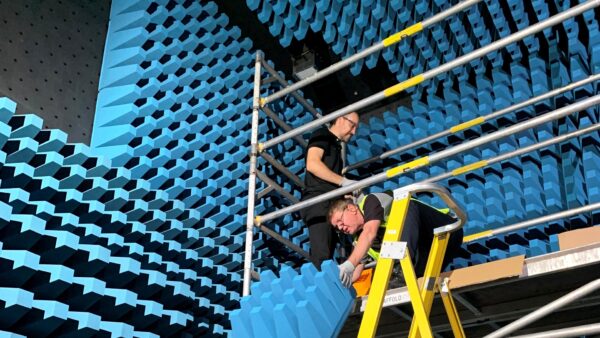 People installing bright blue radio frequency absorbers inside an electronics testing lab.