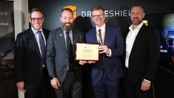 Four men in suits, with one holding a plaque in front of him