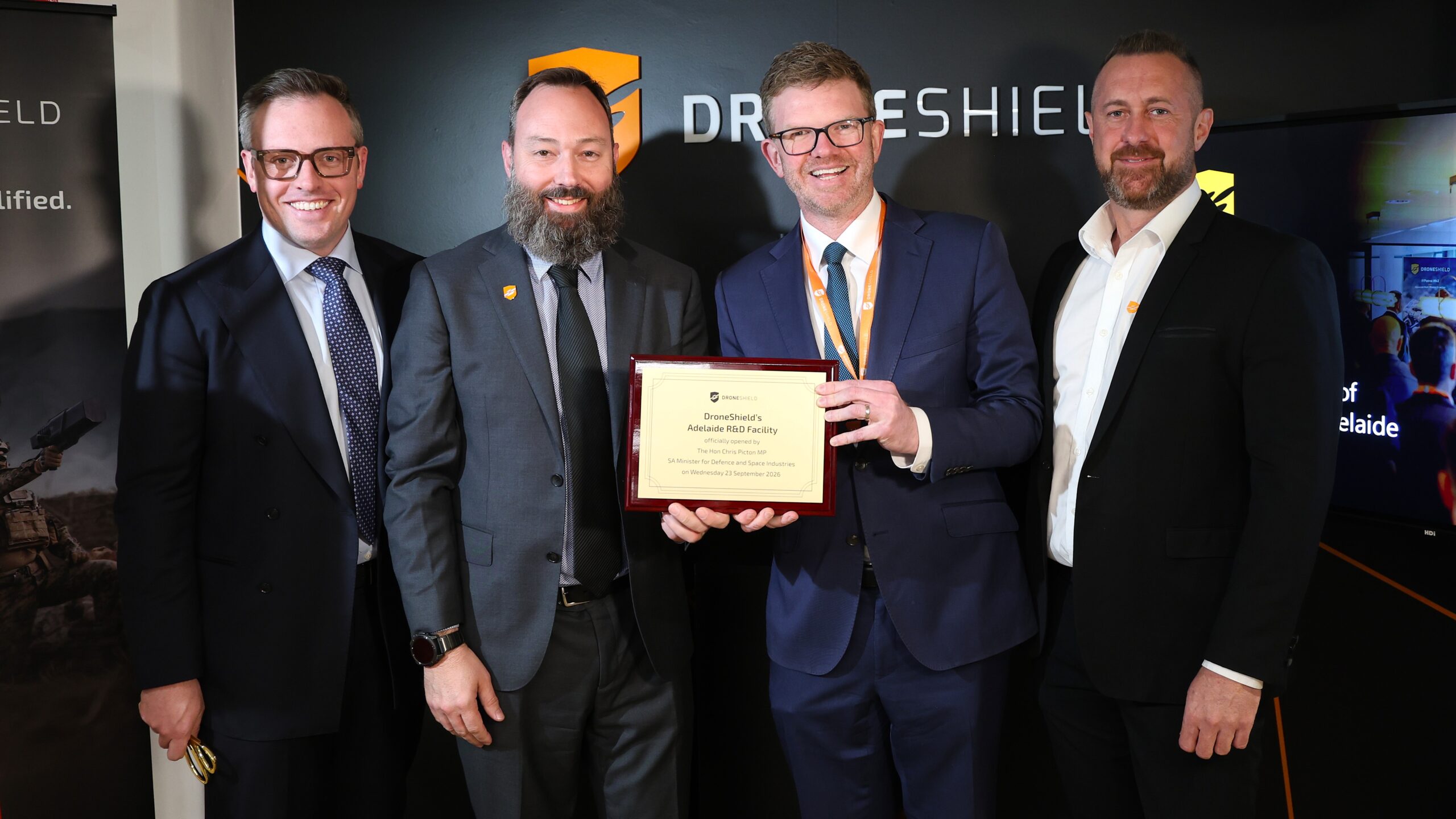 Four men in suits, with one holding a plaque in front of him