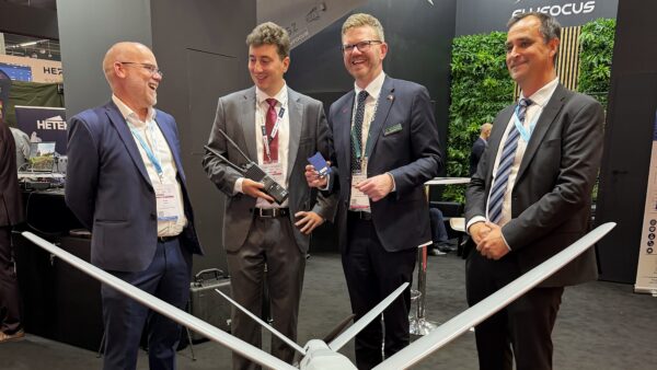 Four men in suits standing in front of a drone at a defence expo