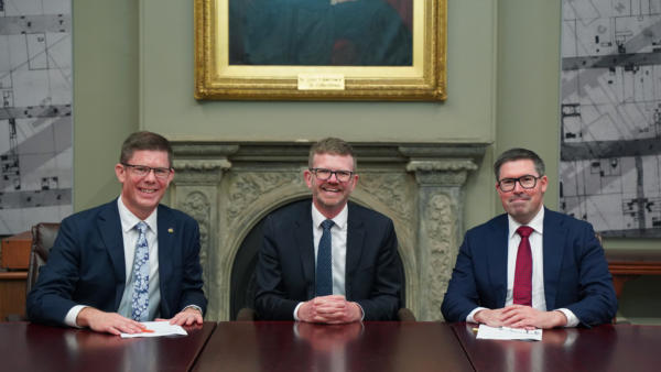 Three men in suits sitting at a desk after an MOU was signed