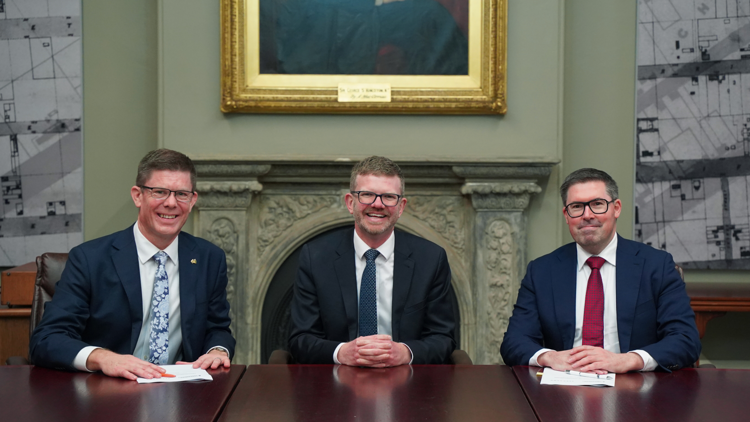Three men in suits sitting at a desk after an MOU was signed