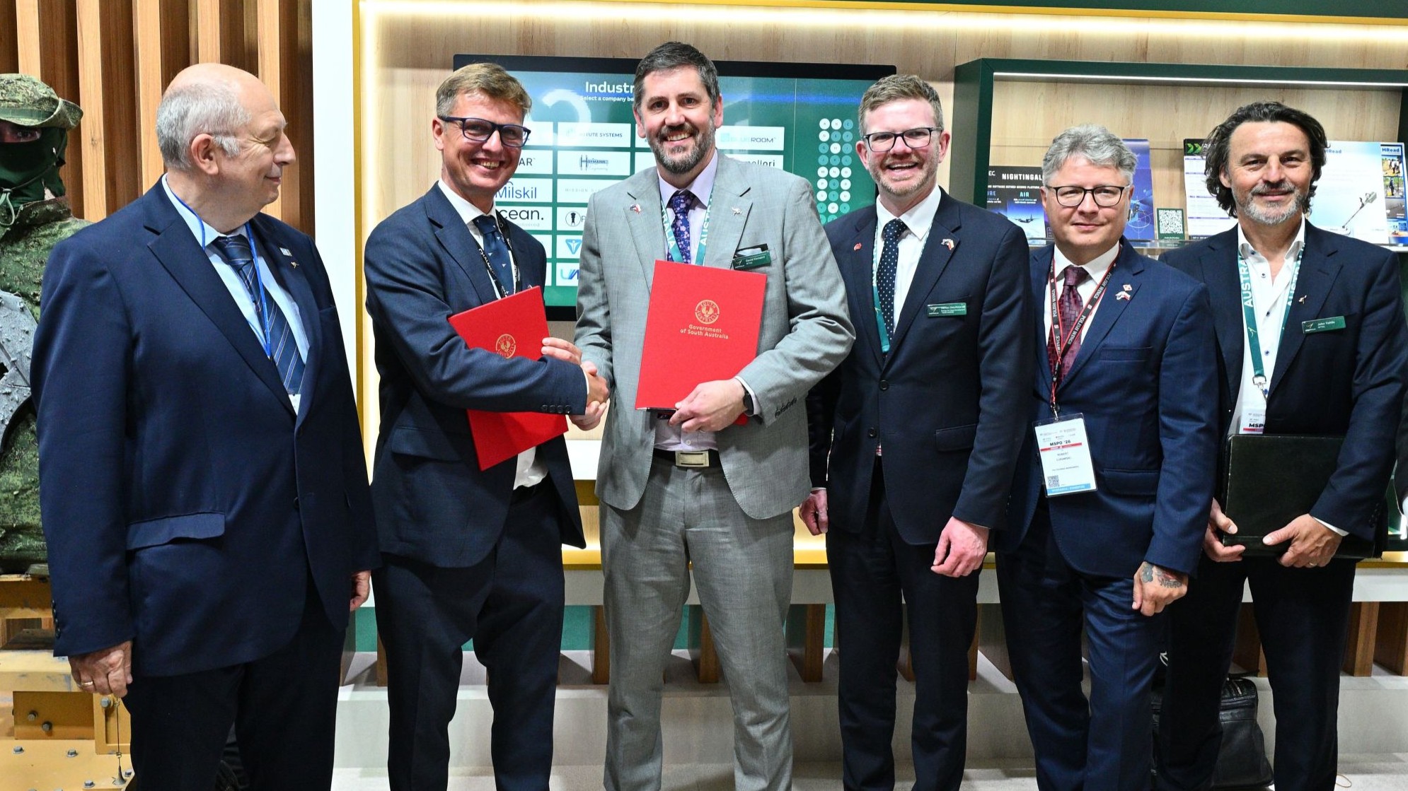RFTEQ and Poland partnership Two men holding red folders shaking hands while other men watch on