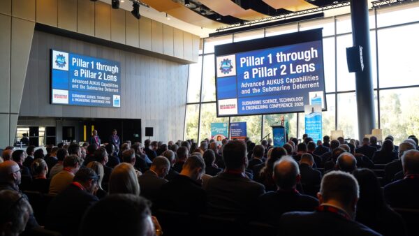 People in a large meeting room with a big screen with white writing on a blue background
