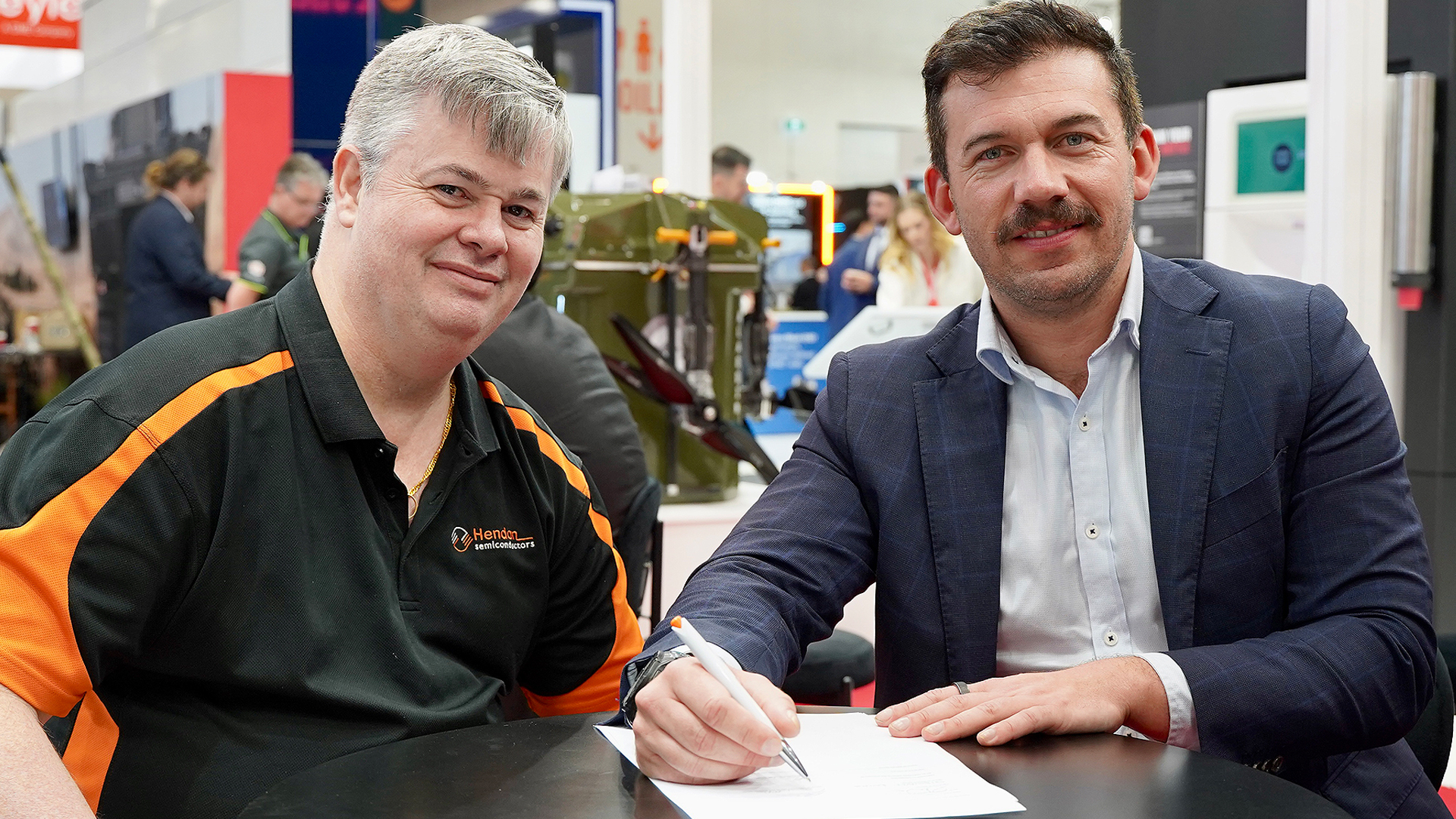 Two men at a defence expo signing an official document.
